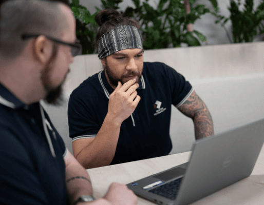 Two men focused on a laptop, collaborating on a project in a modern office environment.