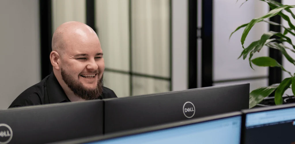 Customer support agent smiling at computer screen in an office setting.